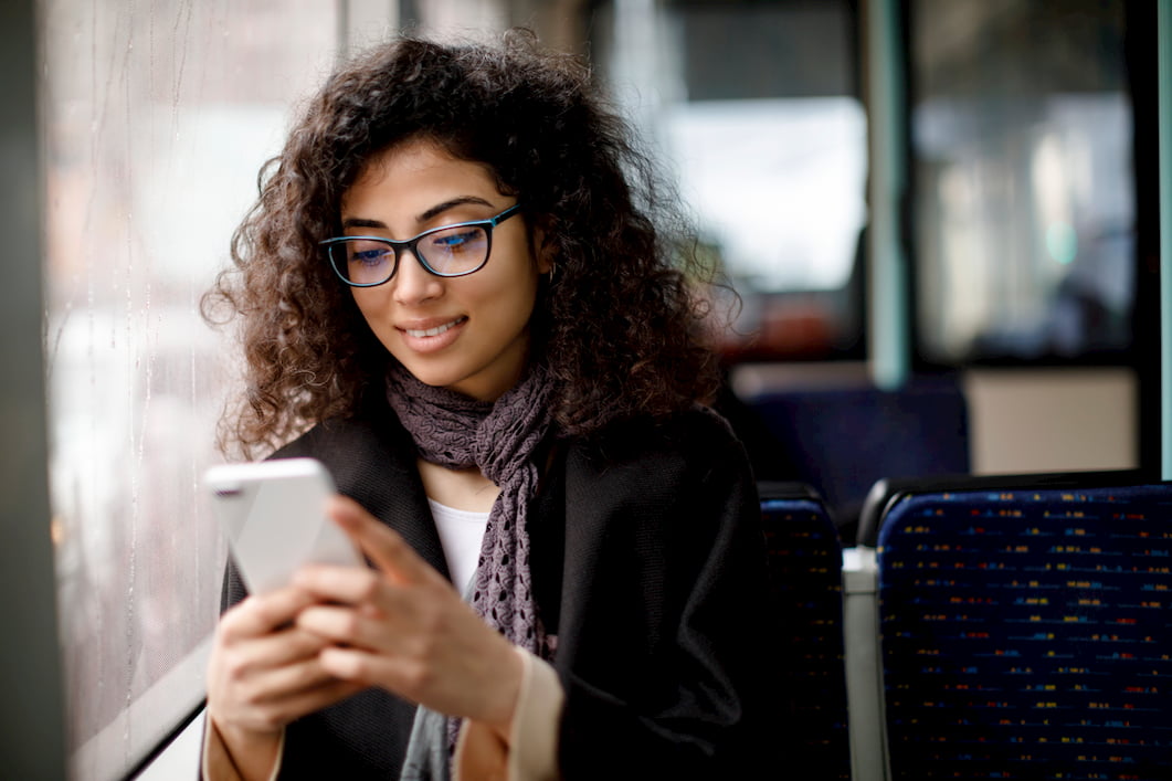 A woman uses her smart phone sitting by the window of a bus