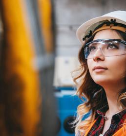 A female engineer in a hard hat looks up at the industrial steel cable reel for a crane in a factory